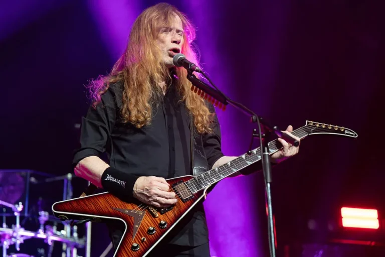 Dave Mustaine sings into a microphone while playing an angular electric guitar.