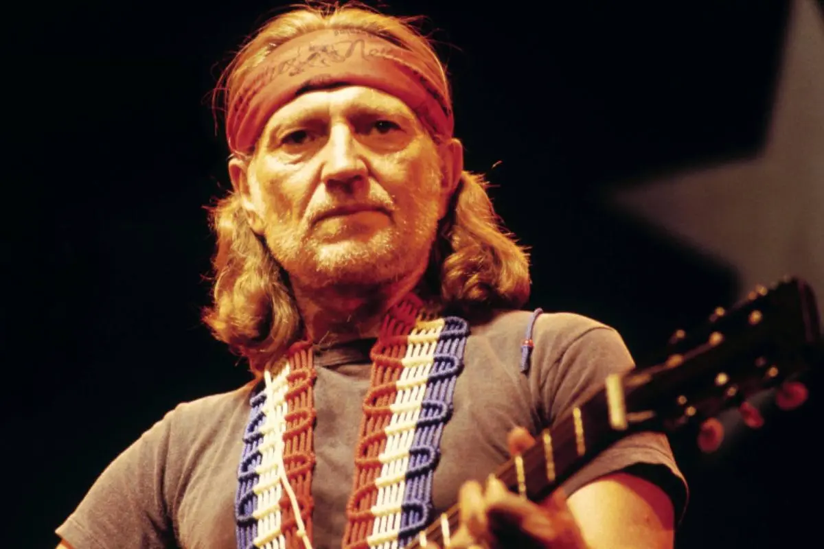 Willie Nelson performing on stage wearing a headband and guitar strap.