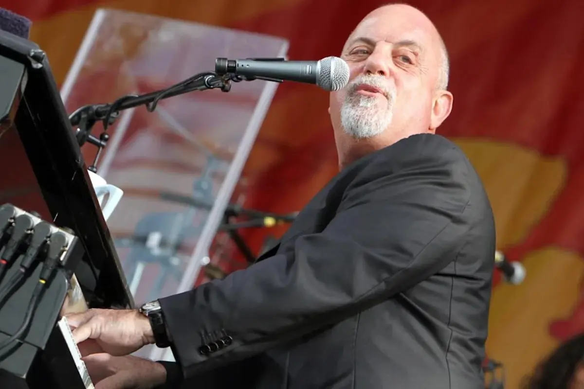 Billy Joel performing onstage, wearing a black suit and playing the piano.