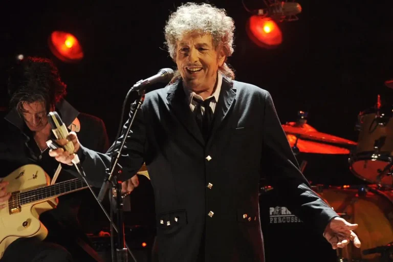 Bob Dylan sings onstage, smiling as he holds a microphone.