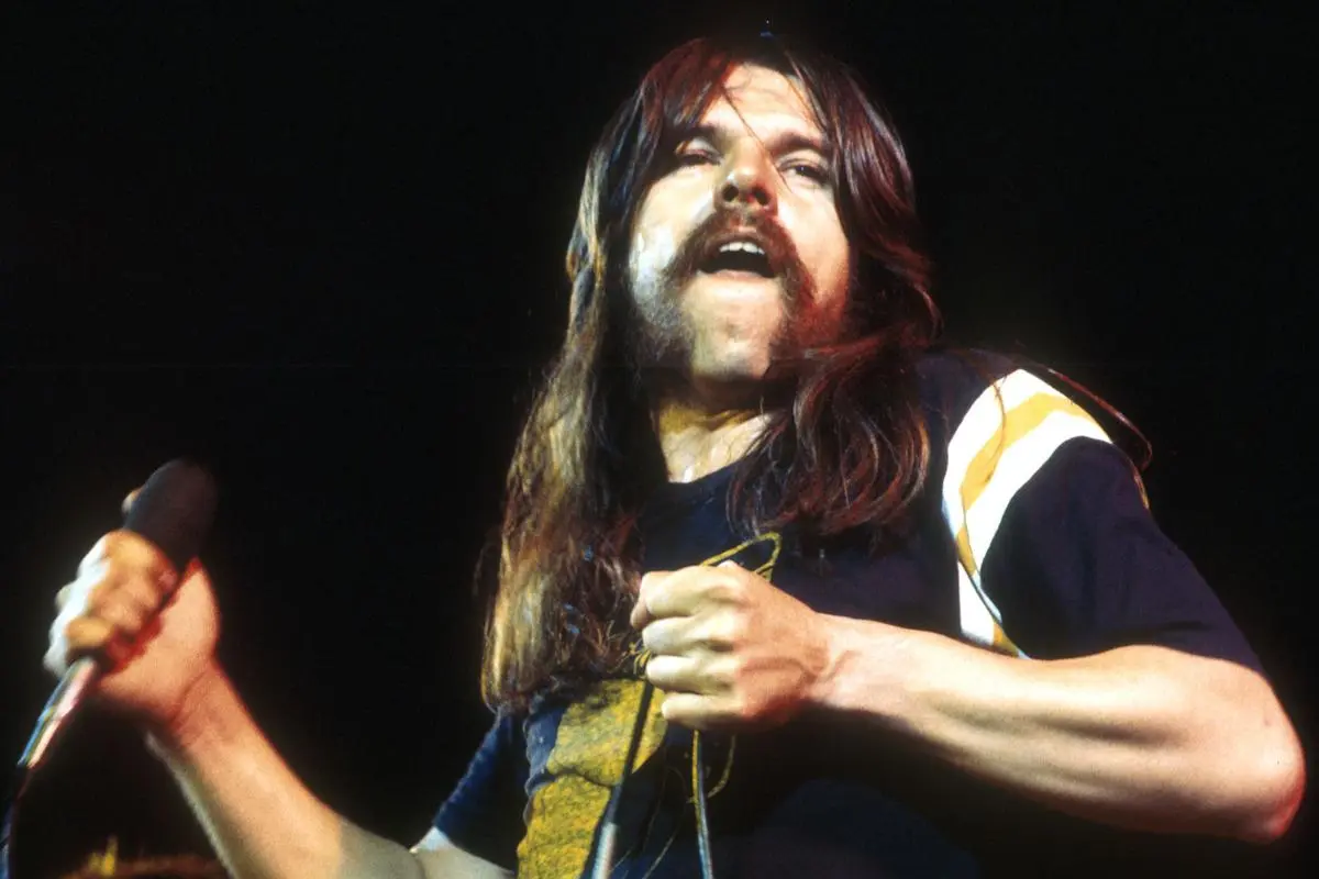 ob Seger performing live on stage, holding a microphone, with long hair and a mustache.