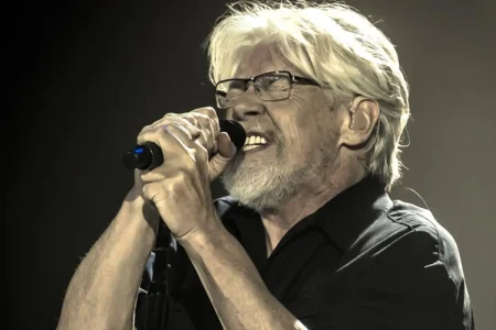 Bob Seger singing into a handheld microphone, wearing glasses and a black shirt.