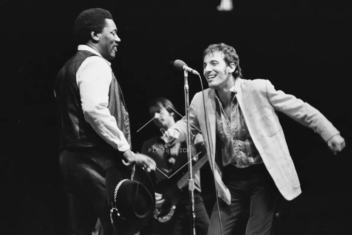 Bruce Springsteen smiles toward Clarence Clemons at a microphone.