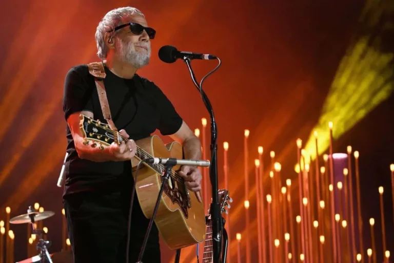 Cat Stevens, performs onstage wearing dark sunglasses and a black shirt.