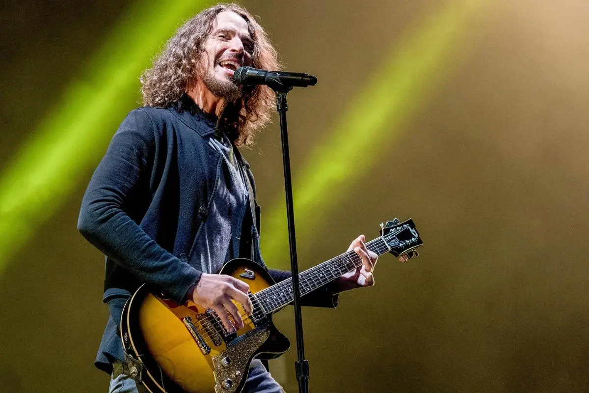 Chris Cornell plays a sunburst electric guitar and sings into a microphone as bright green stage lights shine behind him.