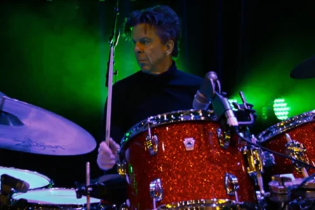chris layton performing live behind a red drum kit with green stage lights.