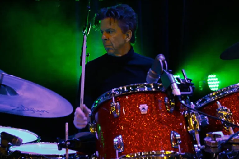 chris layton performing live behind a red drum kit with green stage lights.