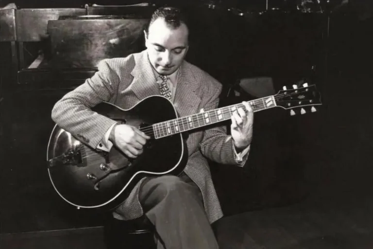 Django Reinhardt seated and playing an acoustic guitar.