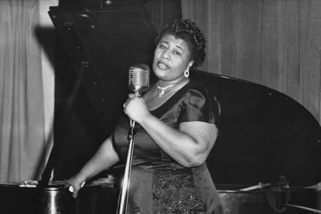 Ella Fitzgerald singing into a microphone beside a grand piano, emphasizing warmth, presence, and expressive storytelling through music.