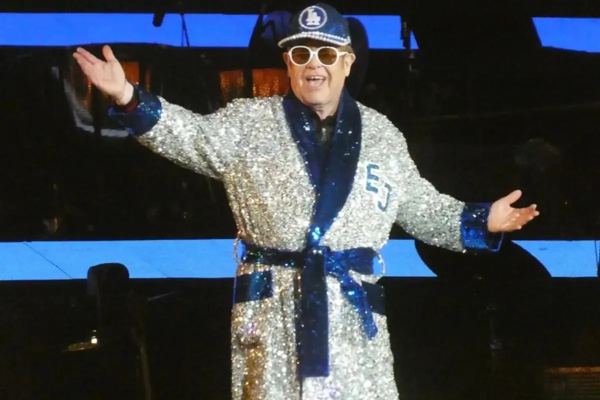 Elton John performs onstage wearing a shimmering silver sequined robe.