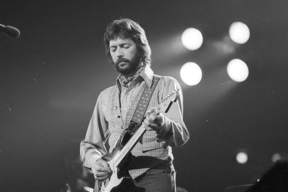 Eric Clapton plays an electric guitar onstage in a black-and-white.