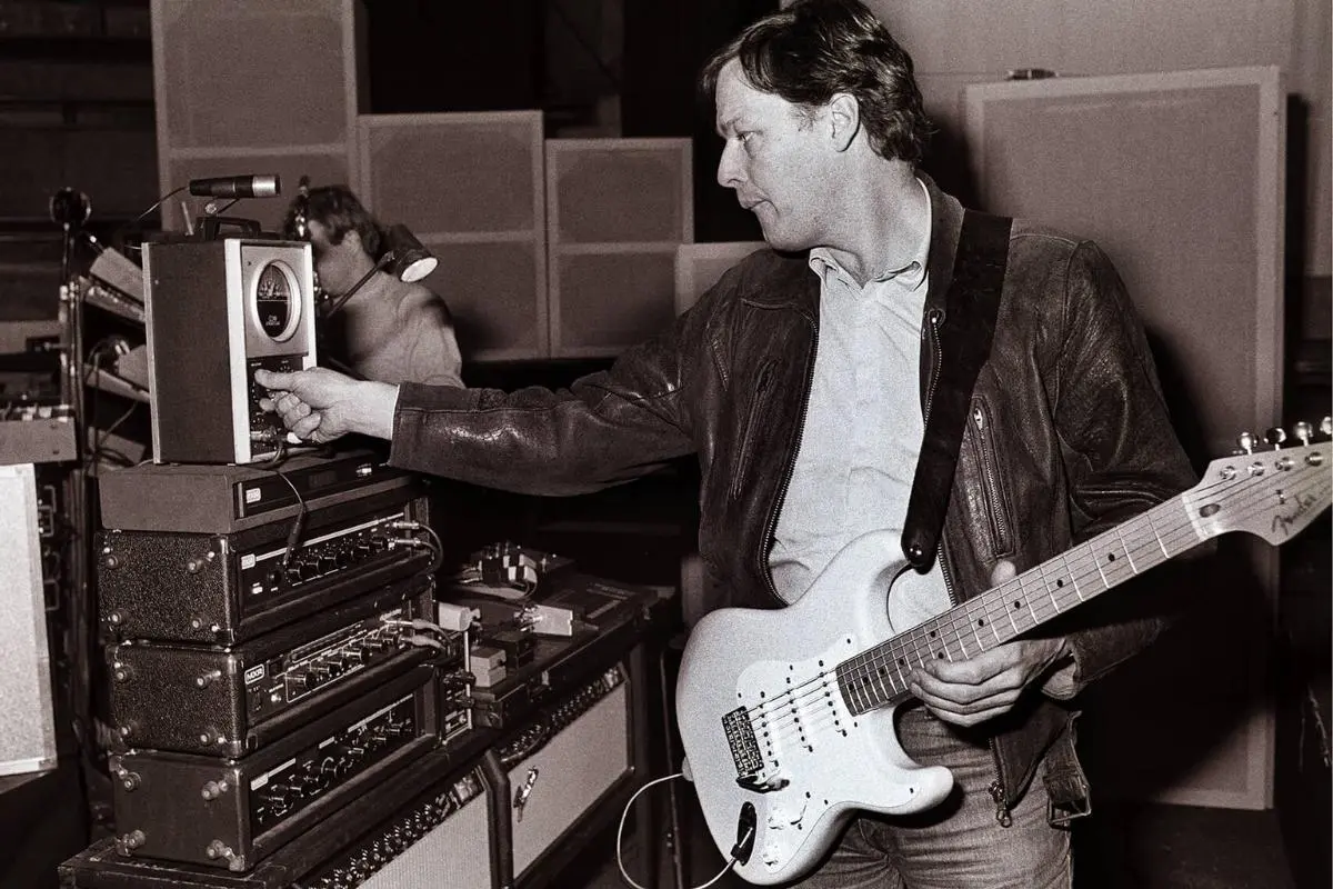 David Gilmour adjusts studio equipment with one hand while holding a white Fender Stratocaster