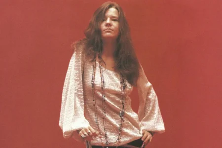 Janis Joplin standing confidently against a solid red backdrop.
