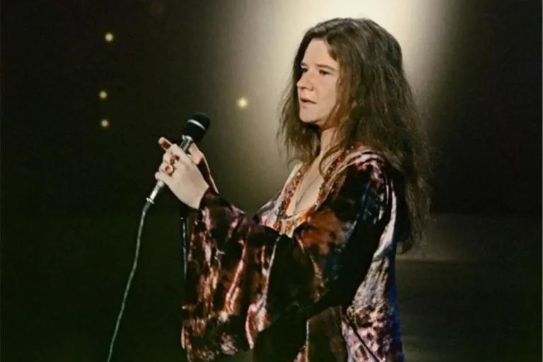 Janis Joplin wears a flowing, patterned top and looks calm and focused as she prepares to sing.