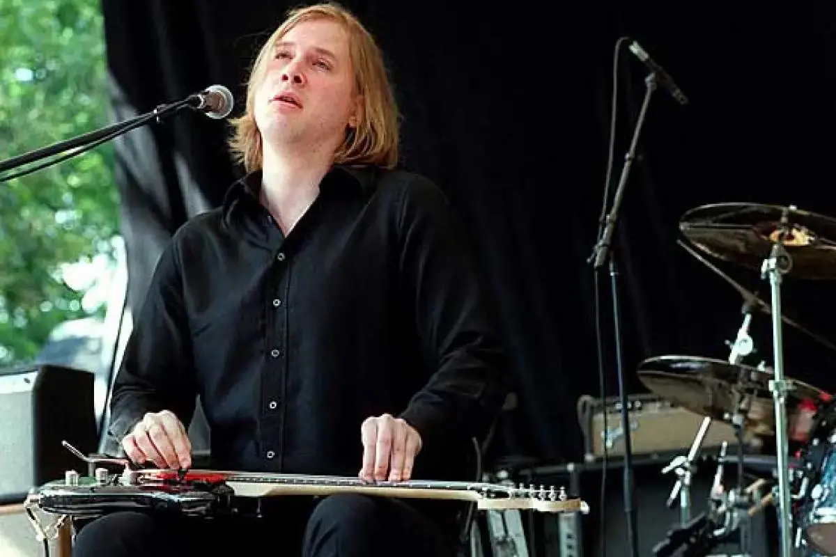 Jeff Healey in a black shirt performs seated onstage, playing a lap steel guitar with an intense expression.