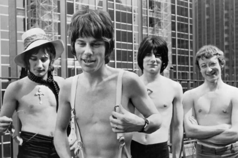 The Jeff Beck Group stand shirtless outdoors near a metal fence.