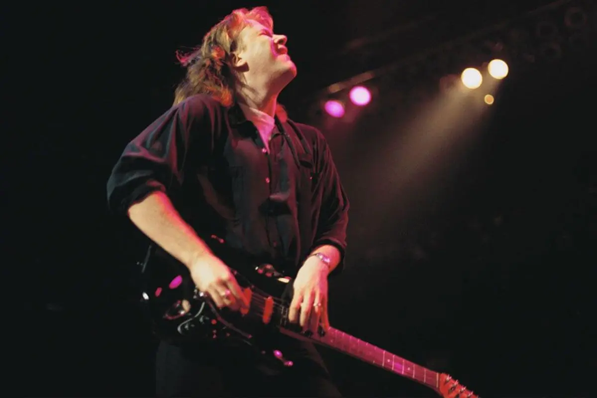 Jeff Healey plays an electric guitar onstage, leaning back with eyes closed. 