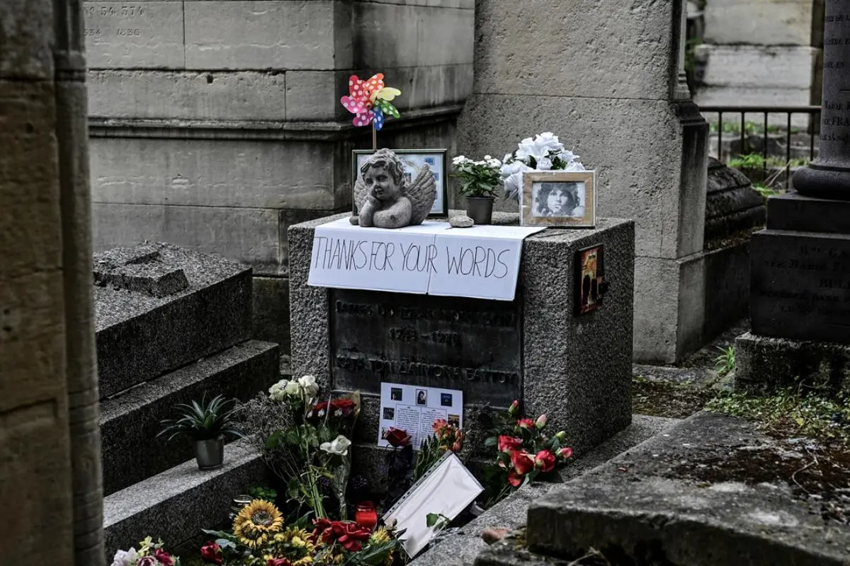 Jim Morrison grave covered with flowers, photos, and a handwritten sign.