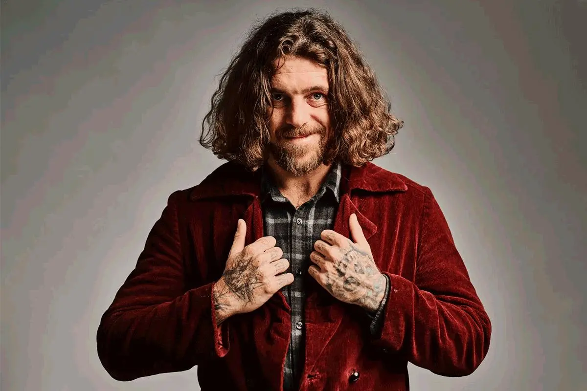 Joe Cocker in a studio portrait wearing a red jacket and smiling.