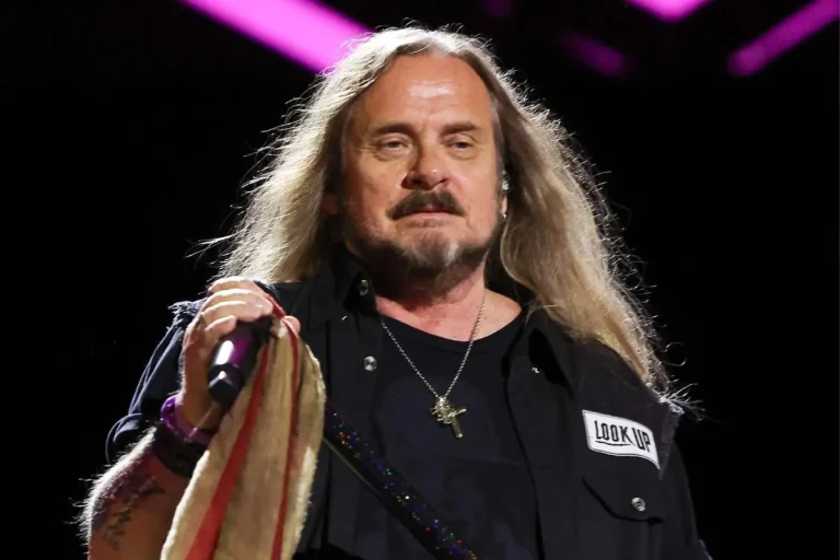 Johnny Van Zant holds a microphone wrapped with a cloth, looking calmly toward the crowd under bright stage lighting.