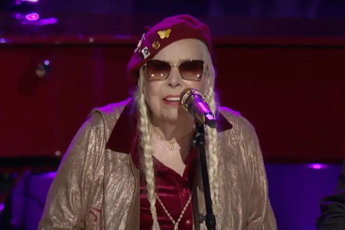 Joni Mitchell performs at a microphone.