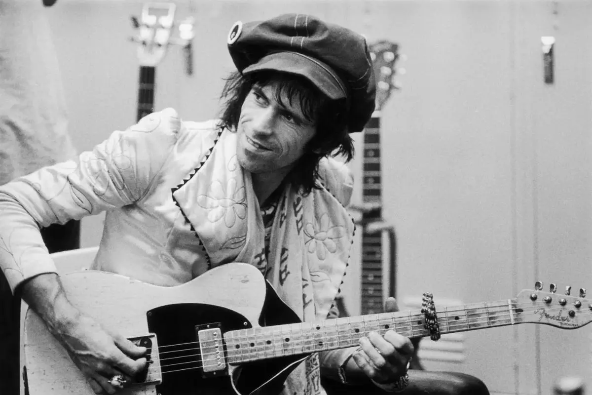 Keith Richards sits holding a worn Fender Telecaster guitar.