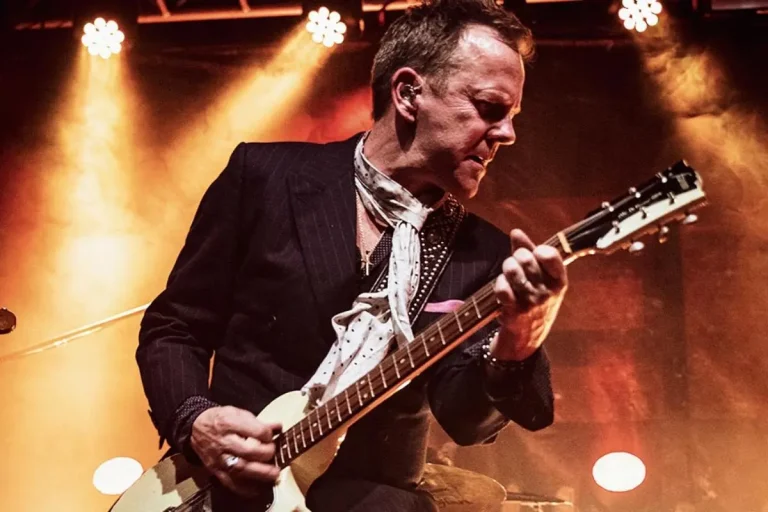 Kiefer Sutherland in concert, playing an electric guitar with intensity.