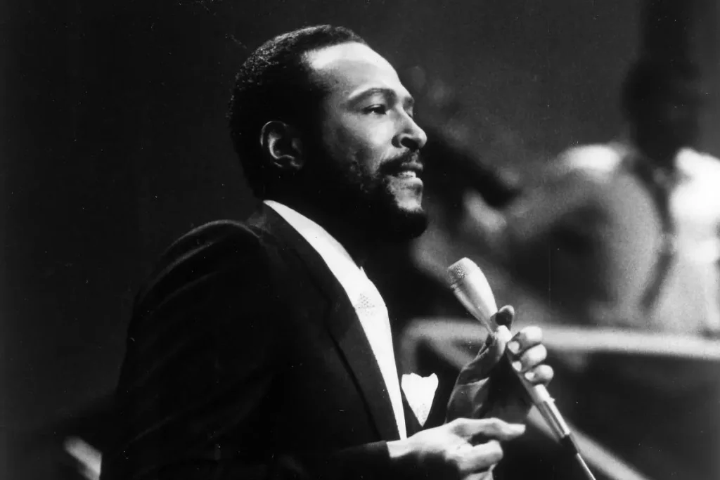 Marvin Gaye performs on stage wearing a dark suit and tie, holding a microphone.