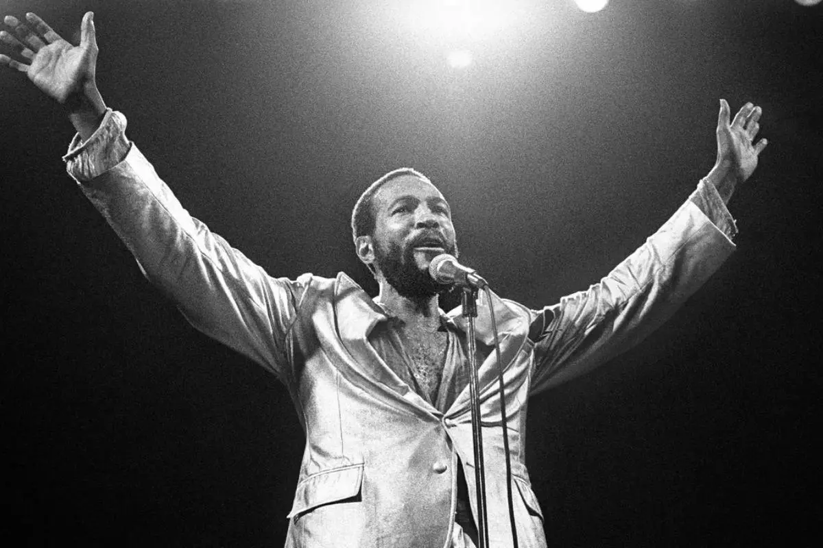 Marvin Gaye stands on stage wearing a shiny jacket.