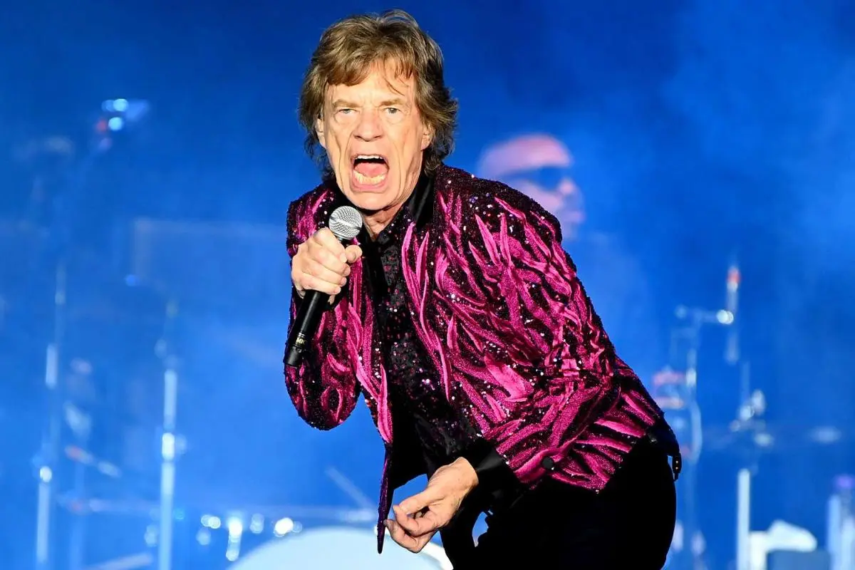 Mick Jagger performing on stage wearing a purple jacket and singing into a microphone.