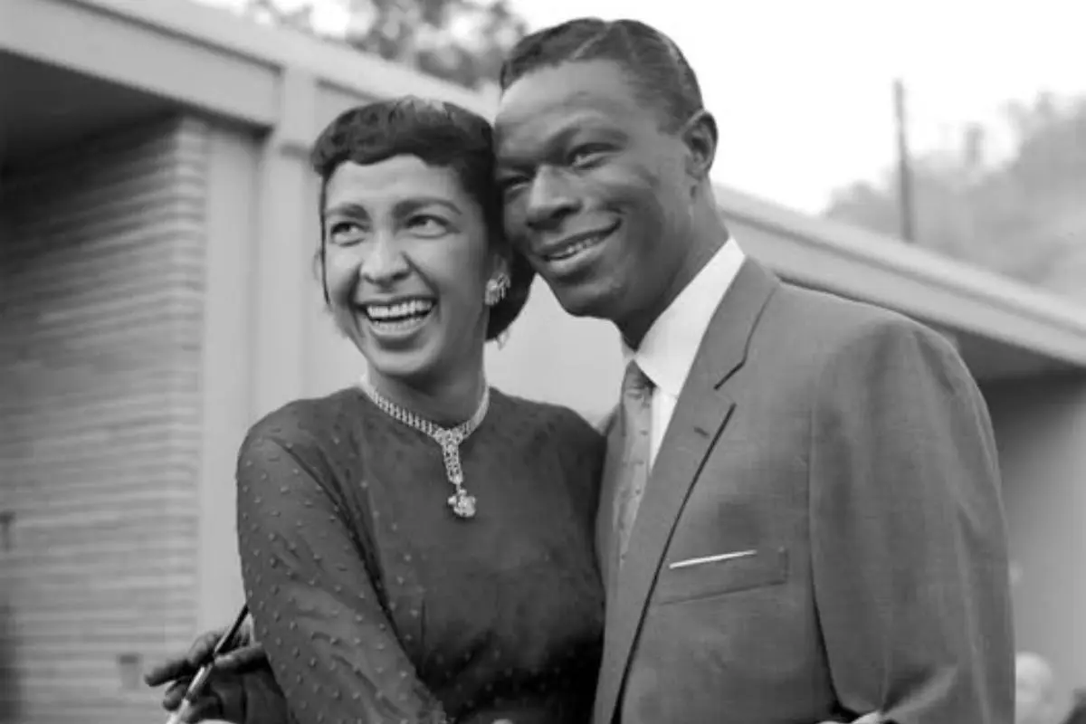 Nat King Cole standing outdoors with his wife, Maria Cole.