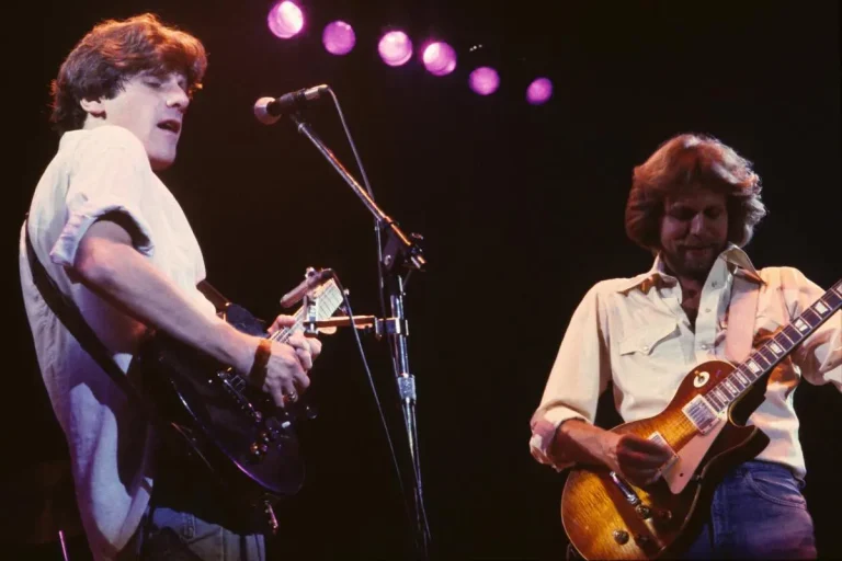 Glenn Frey and Don Felder performing on stage, each playing electric guitars under purple stage lights.