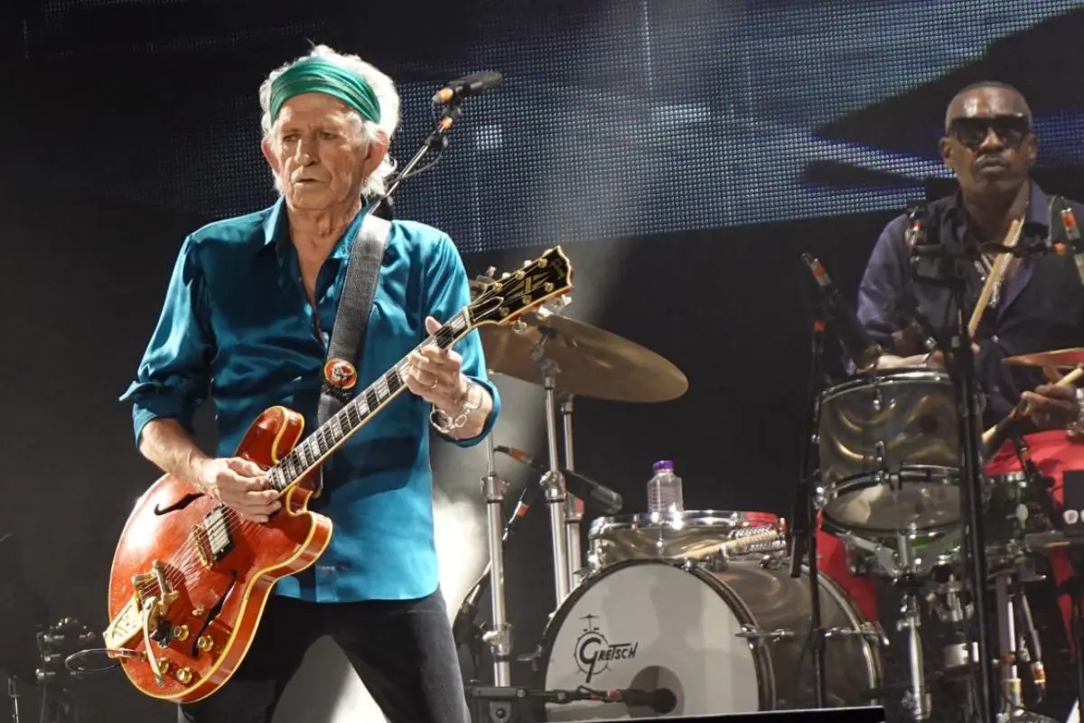 Keith Richards performs onstage wearing a teal shirt and a green headband.