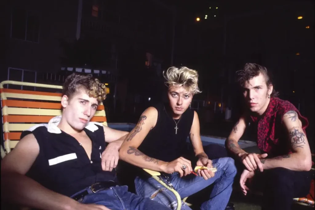 The Stray Cats band members seated together outdoors in a casual group portrait. The Stray Cats posing with instruments in an early band photo.