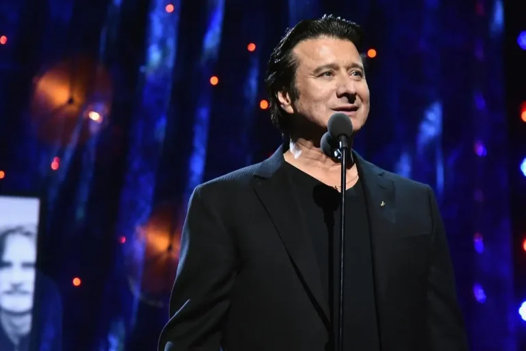 Steve Perry standing at a microphone on stage during a live performance.