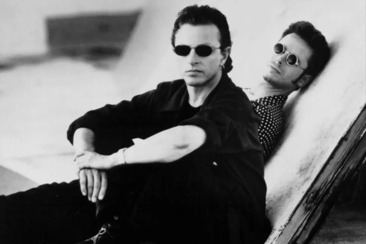 The Rembrandts sit and lean against a slanted surface in a black-and-white promotional photo.