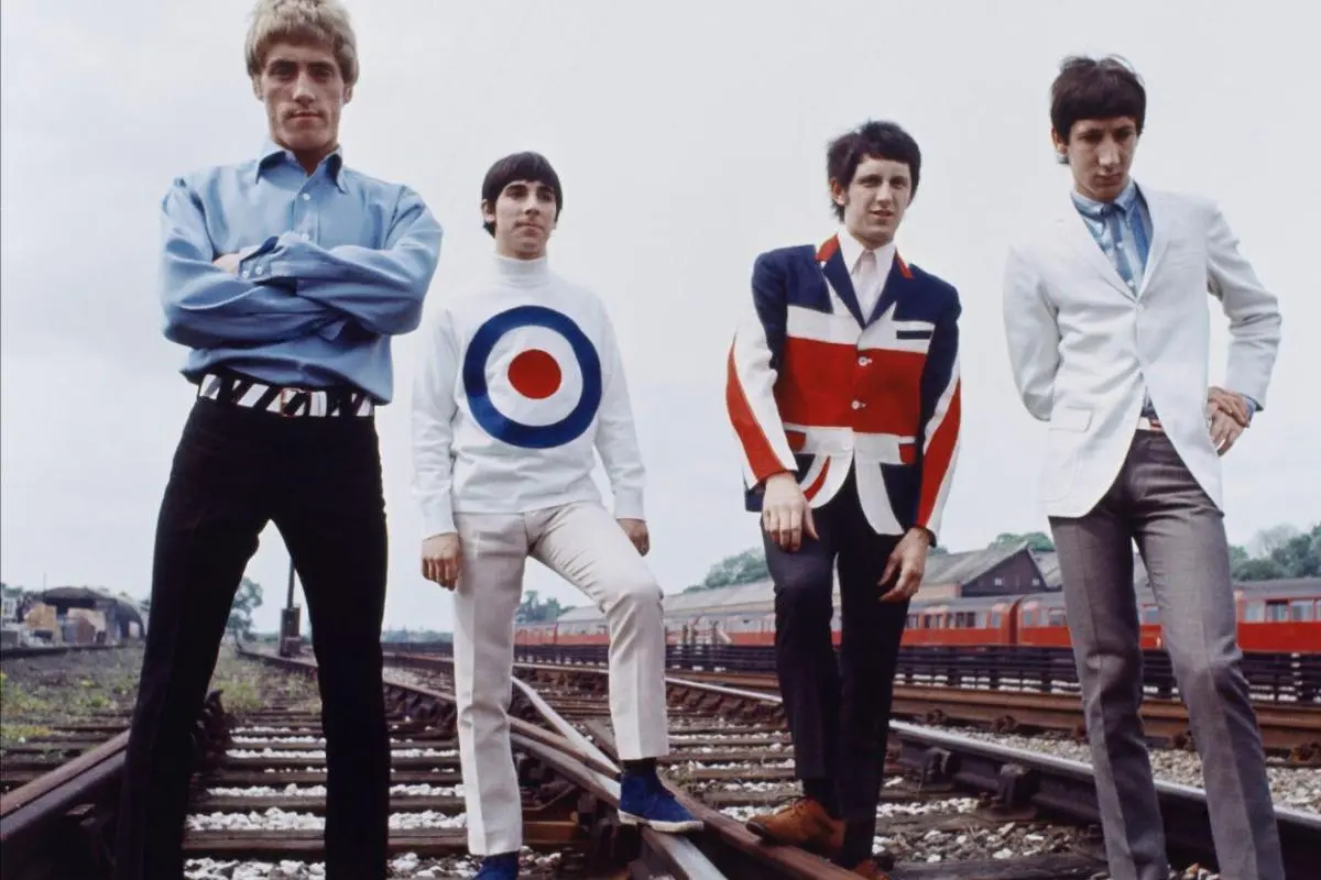 Pete Townshend, Roger Daltrey, John Entwistle, and Keith Moon standing on railway tracks wearing Mod-era outfits.