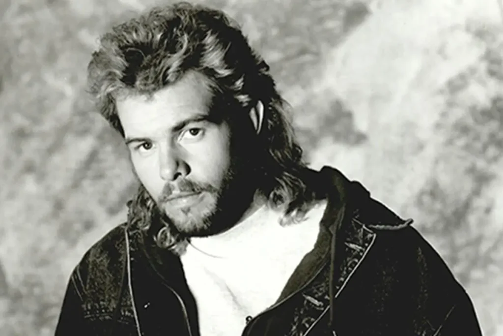 Tony Keith sings into a microphone while playing a red acoustic guitar during a live concert.