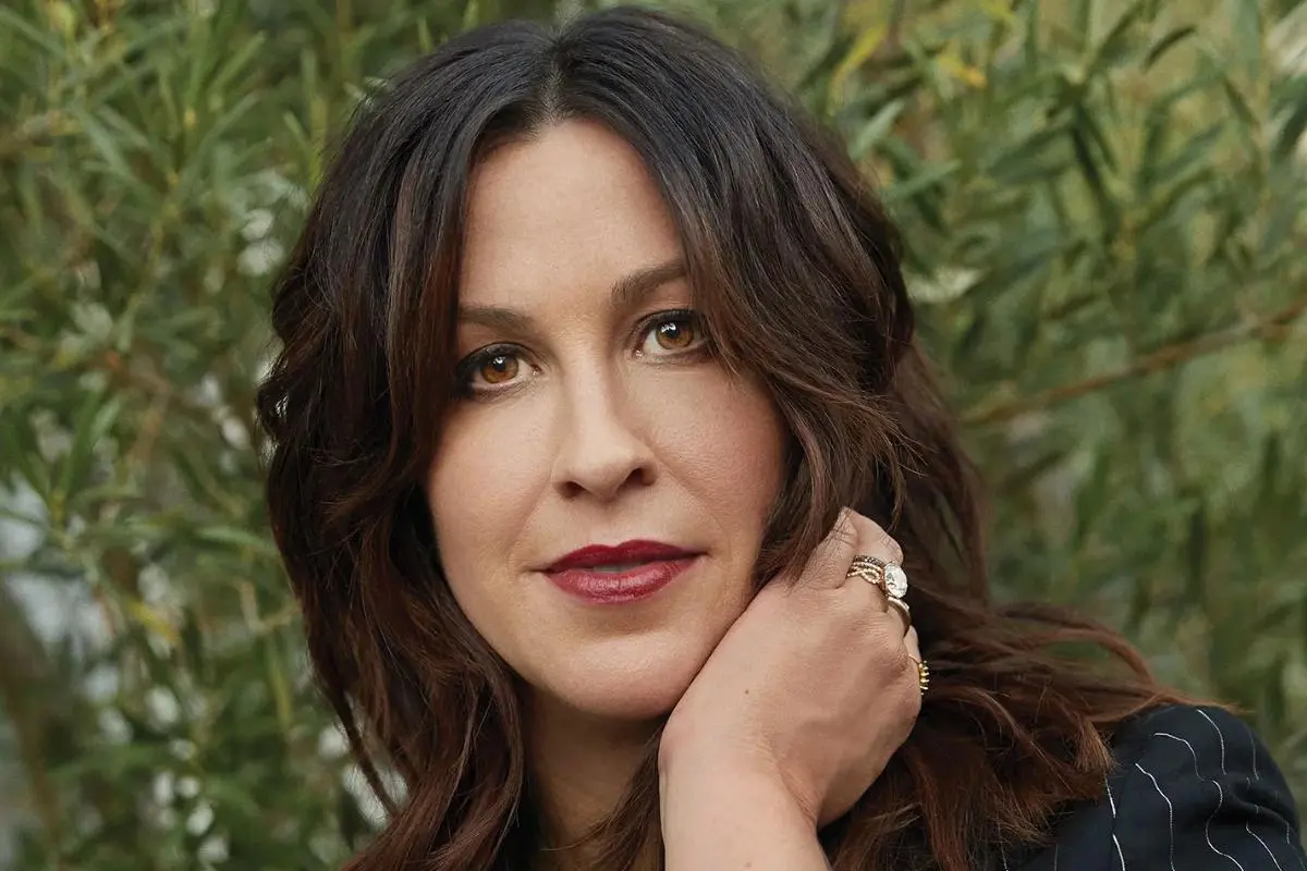 Alanis Morissette outdoor portrait with wavy dark hair, wearing subtle makeup and looking directly at the camera.
