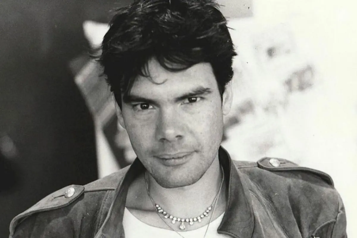 Alphaville with dark hair and a serious expression, wearing a casual jacket and layered necklaces.