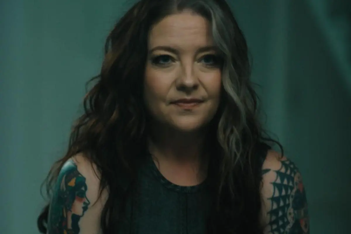 Ashley McBryde in a close-up portrait, with long dark hair featuring a gray streak, wearing a sleeveless black top.