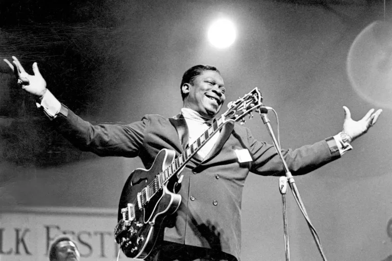 B.B. King performing on stage with arms outstretched, smiling as he holds his guitar, capturing the joy and showmanship of his live blues performances.