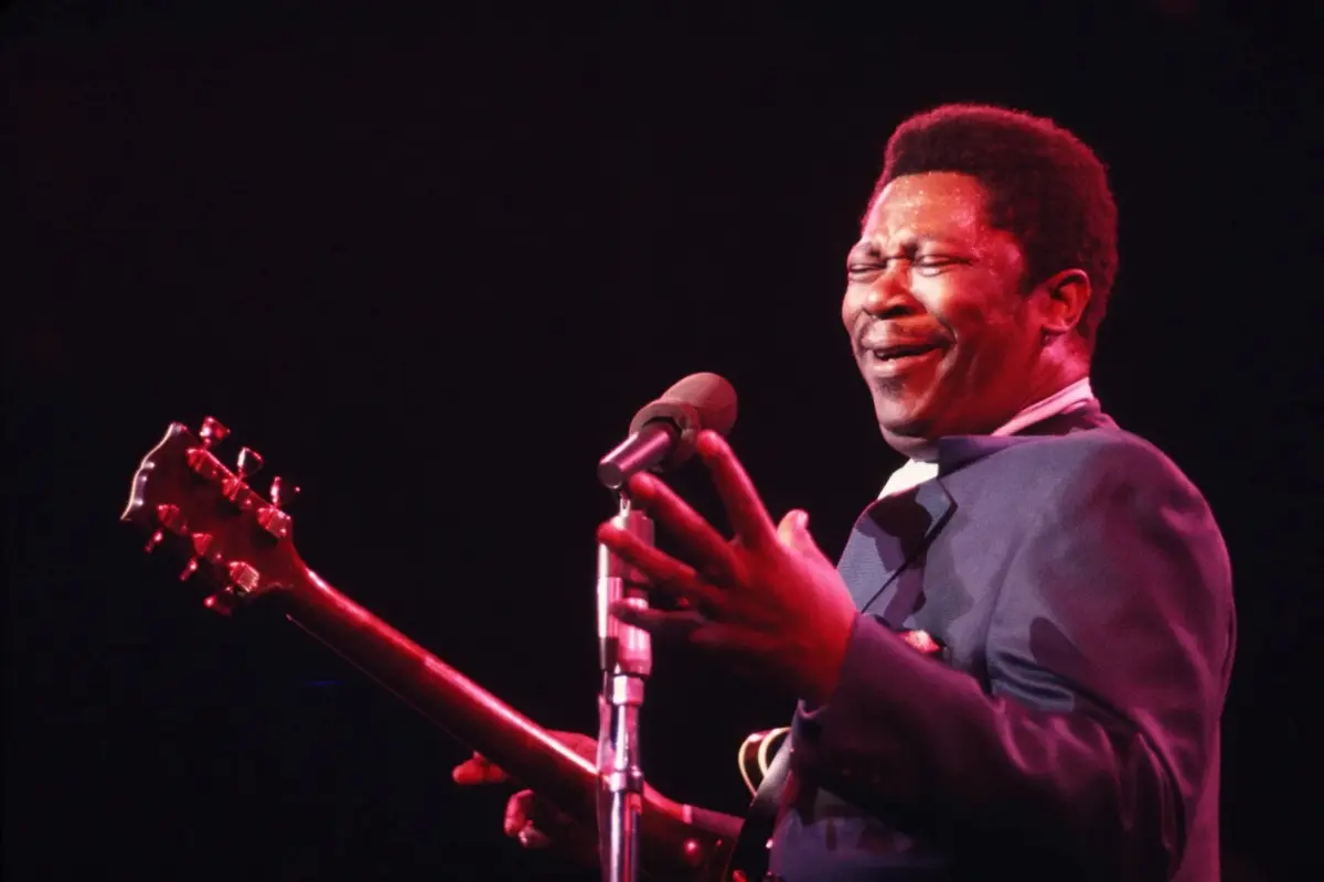 B.B. King singing into a microphone while holding his guitar under stage lights, conveying the passion and soul of his live concert presence.