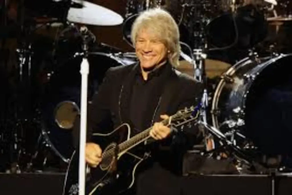 Bon Jovi smiling while playing guitar on stage during a live concert performance.