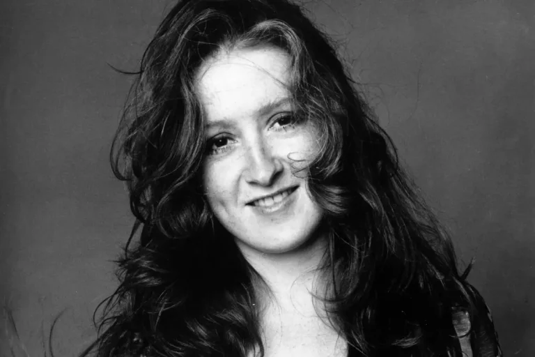 Black-and-white portrait of a young Bonnie Raitt, smiling softly with loose hair framing her face.