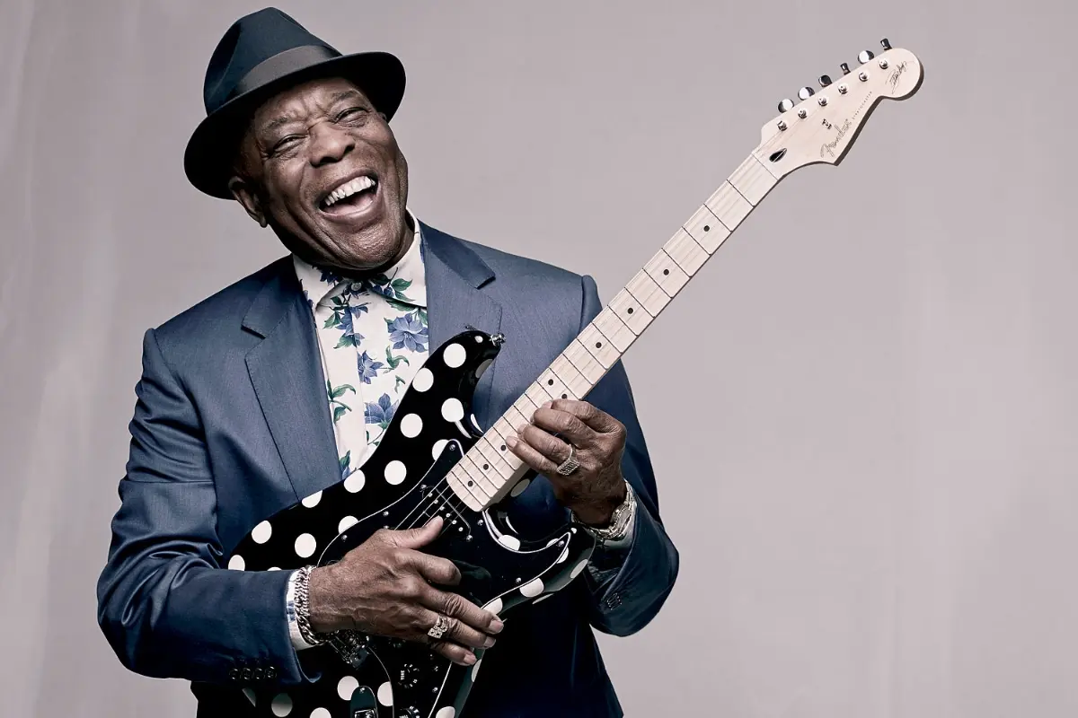Buddy Guy laughs while playing a polka-dot electric guitar, reflecting his vibrant personality and iconic status in blues history.