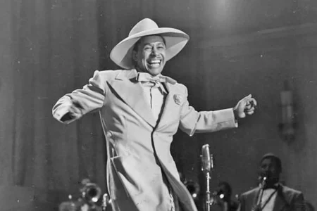 Cab Calloway dancing energetically with a big smile while a microphone and band members appear in the background.