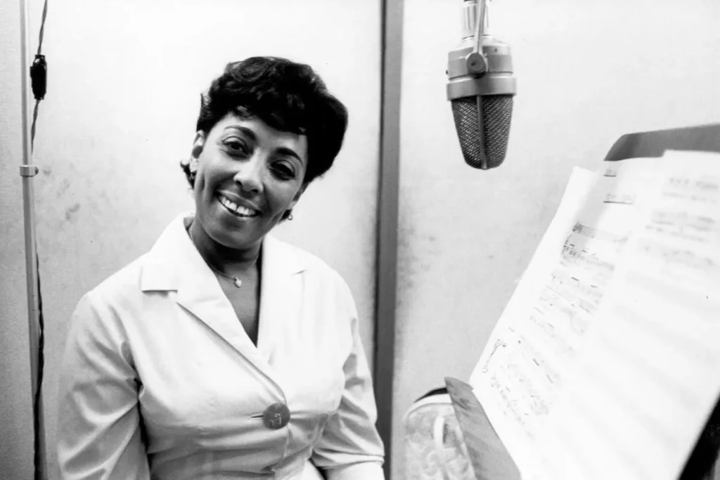 Carmen McRae: The Quiet Voice That Cut Loudest in Jazz Carmen McRae smiling in a recording studio, standing beside a large vintage microphone.