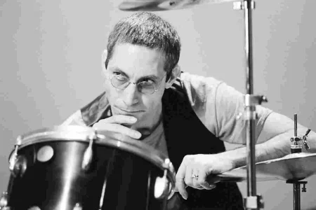 Charlie Watts seated at a drum kit in a black-and-white portrait, wearing glasses.
