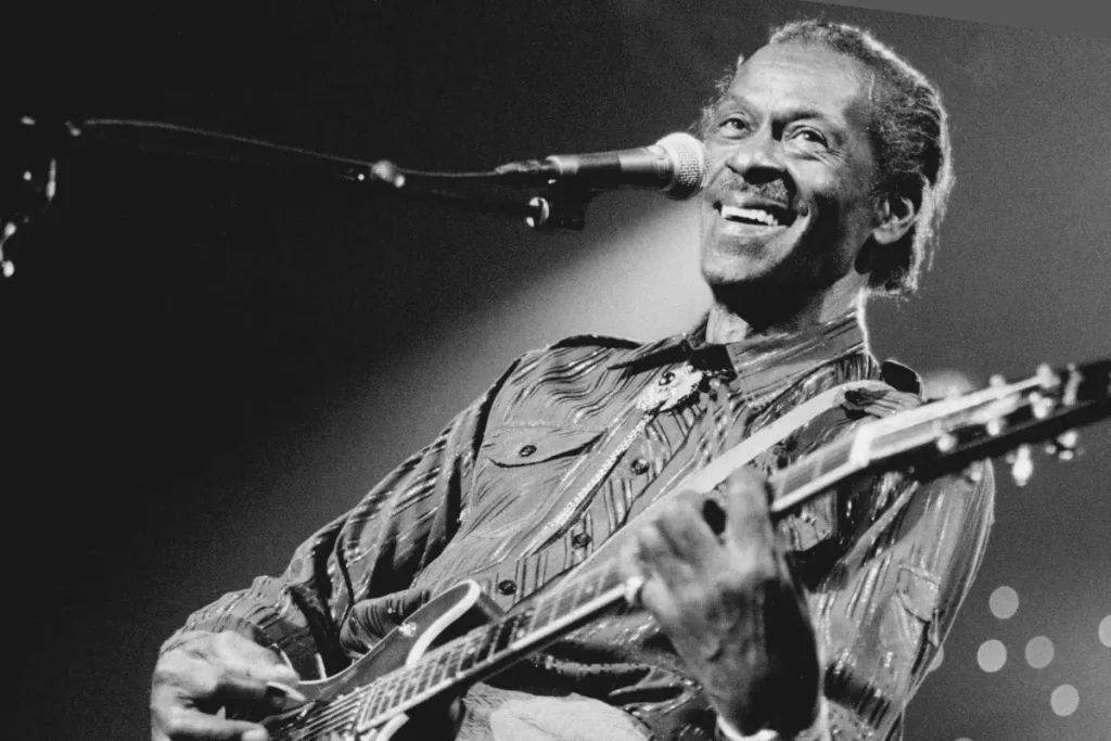 Chuck Berry smiling guitarist singing into a microphone while playing on stage, conveying joy, confidence, and lasting influence in live rock music.